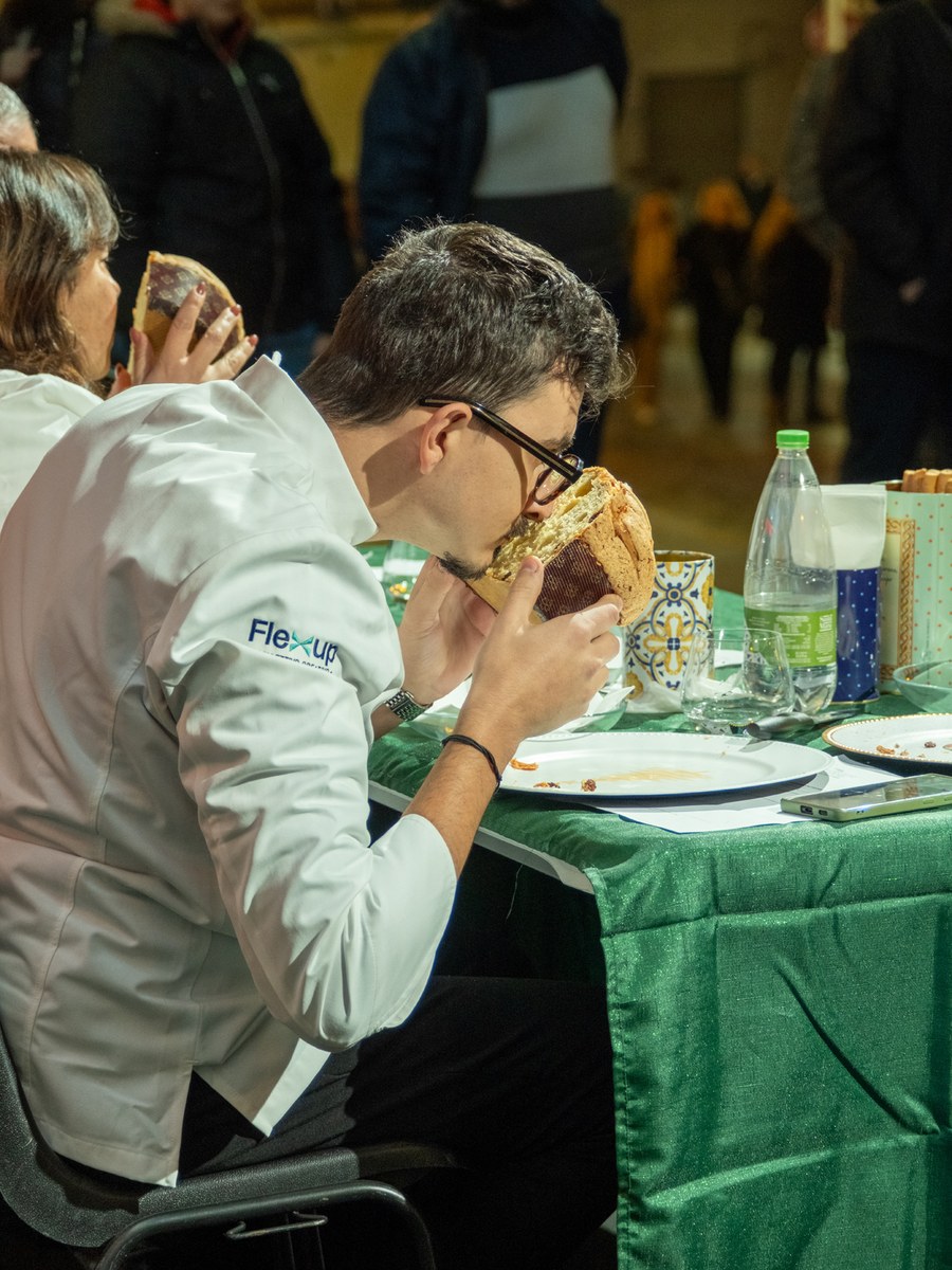 Maestro pasticcere in giacca bianca che annusa una porzione di panettone al tavolo dell'assaggio